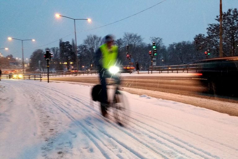 Cyklist cyklar på snöig cykelbana. Bilist syns i bildens högerkant.