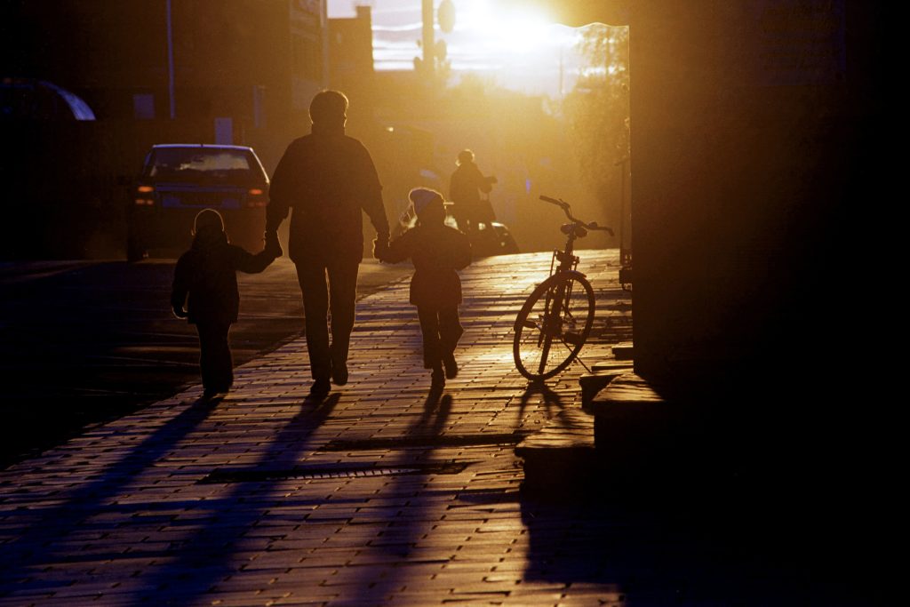 En vuxen och två barn promenerar i ett varmt gulbrunt höstljus.