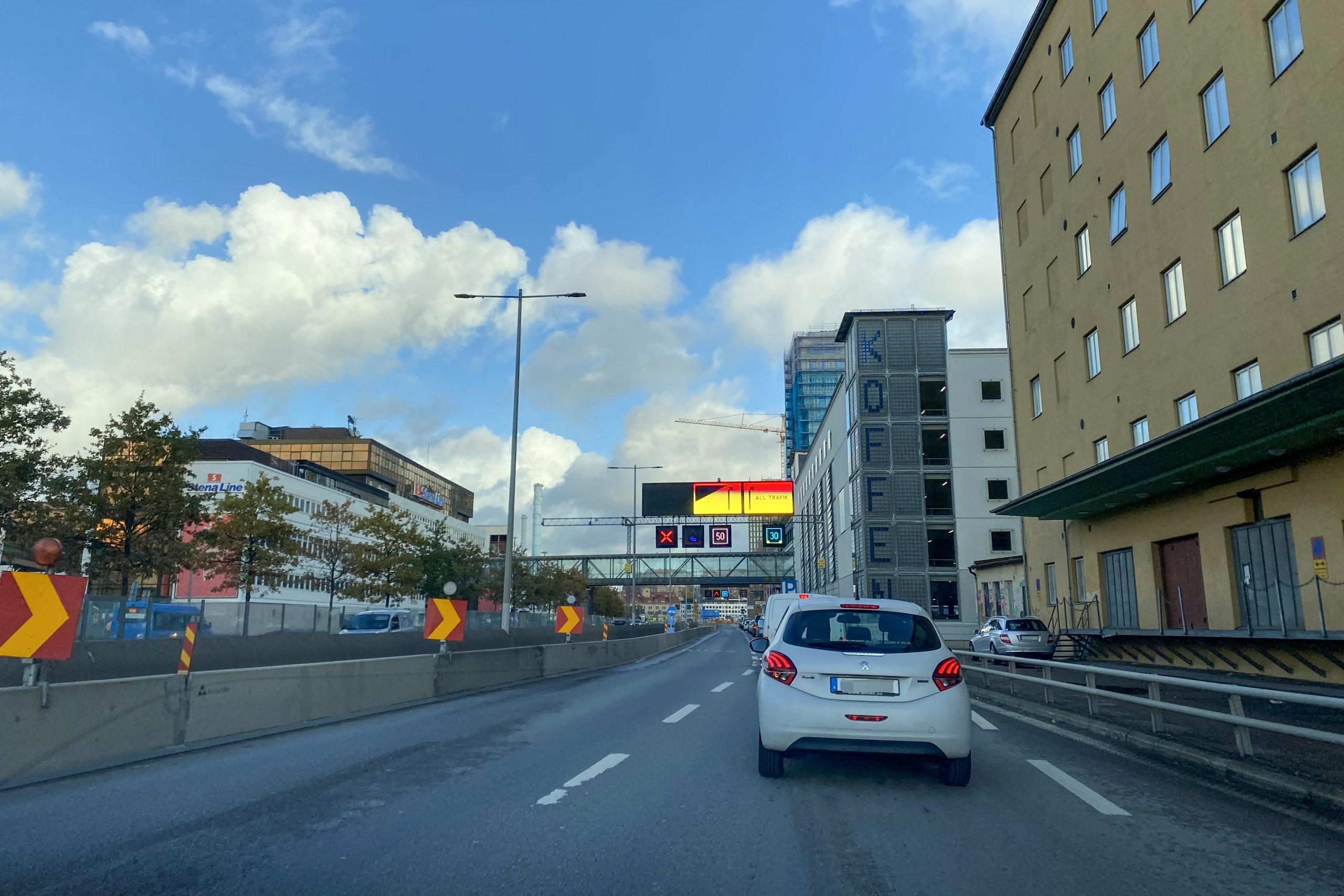 Två bilar syns köra från Cronackersgatan mot rondellen i Eriksbergsmotet. E gångtrafikant går på Cronackersbron mot Lindholmen.