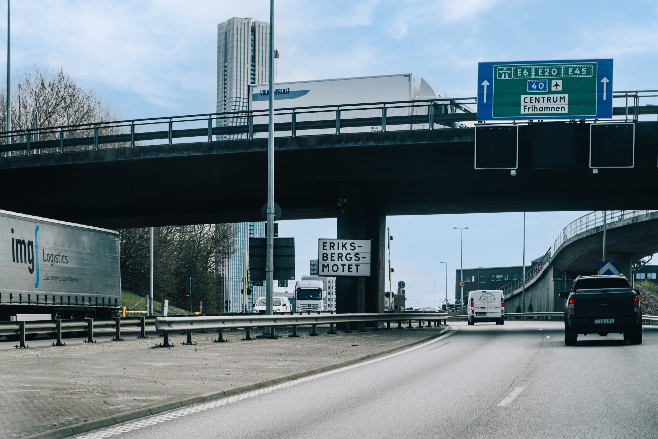 Två bilar syns köra från Cronackersgatan mot rondellen i Eriksbergsmotet. E gångtrafikant går på Cronackersbron mot Lindholmen.