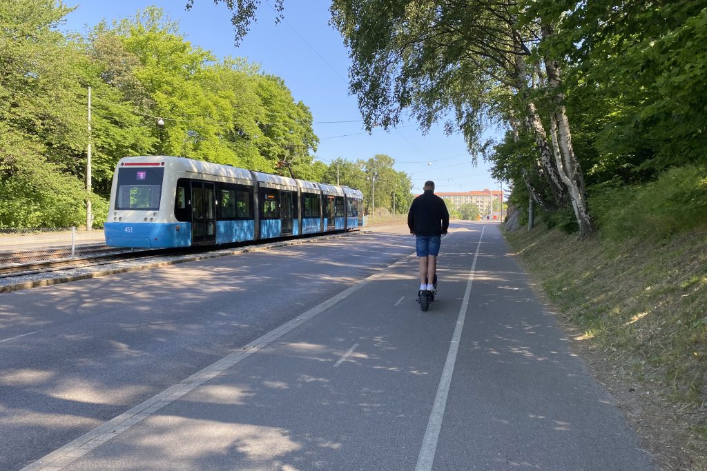 Bredvid en spårvagn åker en man på en elsparkcykel.