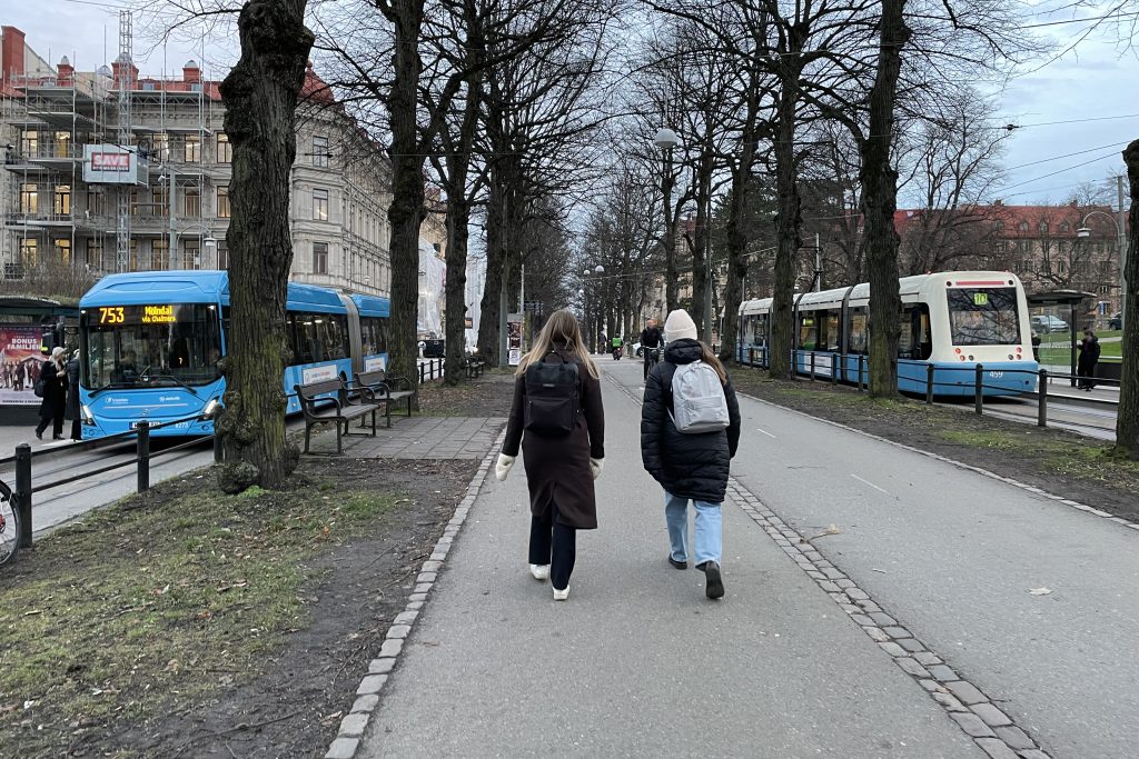 Promenerande vänner en decemberdag vid Vasaplatsens hållplats där en buss och spårvagn släpper på resenärer.