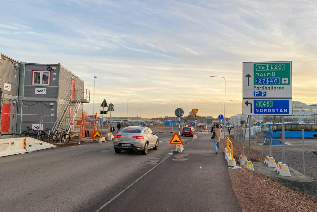 Personbilar kör längs Kruthusgatan med gående på trottoaren till höger och vägskyltar mot Nordstan och Malmö.