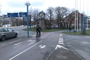 En cyklist är på väg att passera genom en cykelpassage. En bil syns till vänster i bilden.