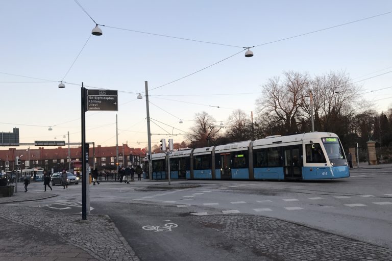 Spårvagn kör från Redbergsplatsen. Gående syns vänster i bild.