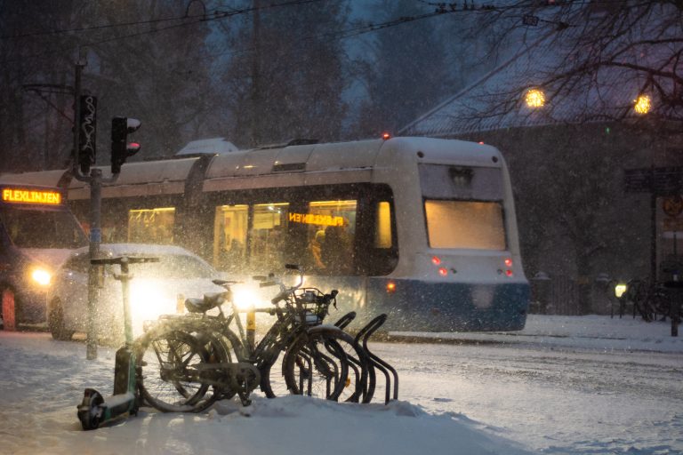 Snön faller över Stigbergstorget och några cyklar lyses upp av förbipasserande bil och spårvagn.